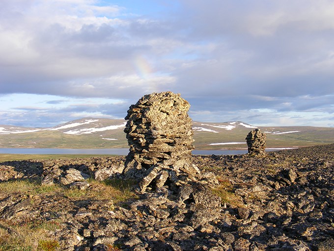 Stone cairns with Kuzitrin Lake in the background and a rainbow in the sky.